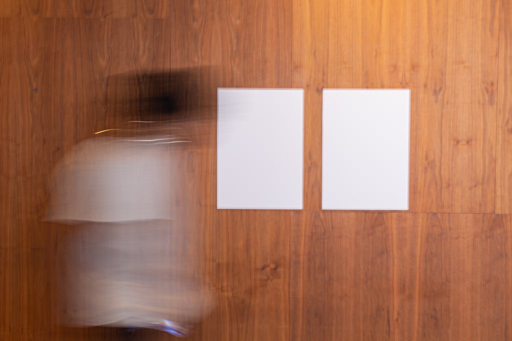 Blurred motion of a person walking past two blank canvases on a wooden wall.
